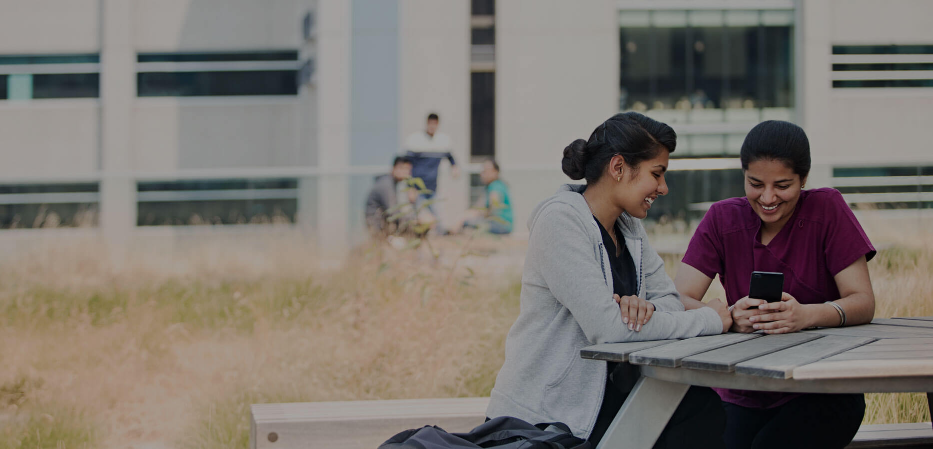 Students sitting on patio looking at smartphone